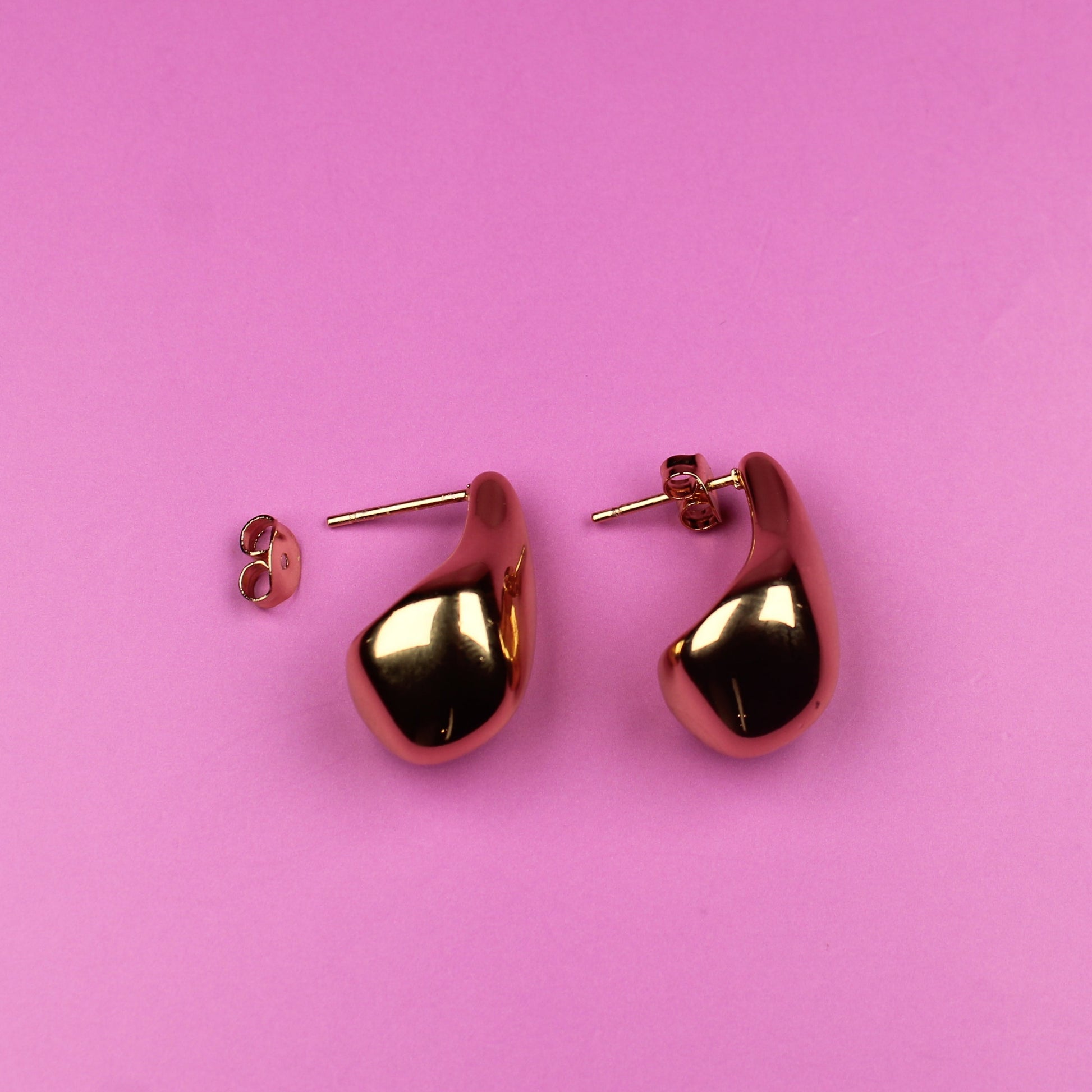 Gold heart-shaped earrings on a pink background
