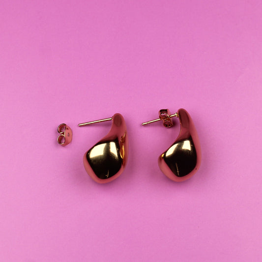 Gold heart-shaped earrings on a pink background