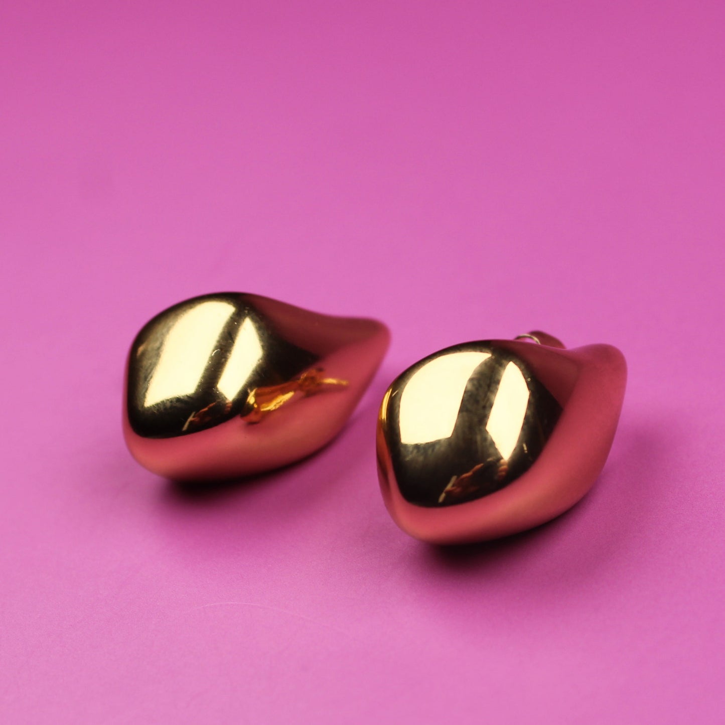 Gold heart-shaped earrings on a pink background