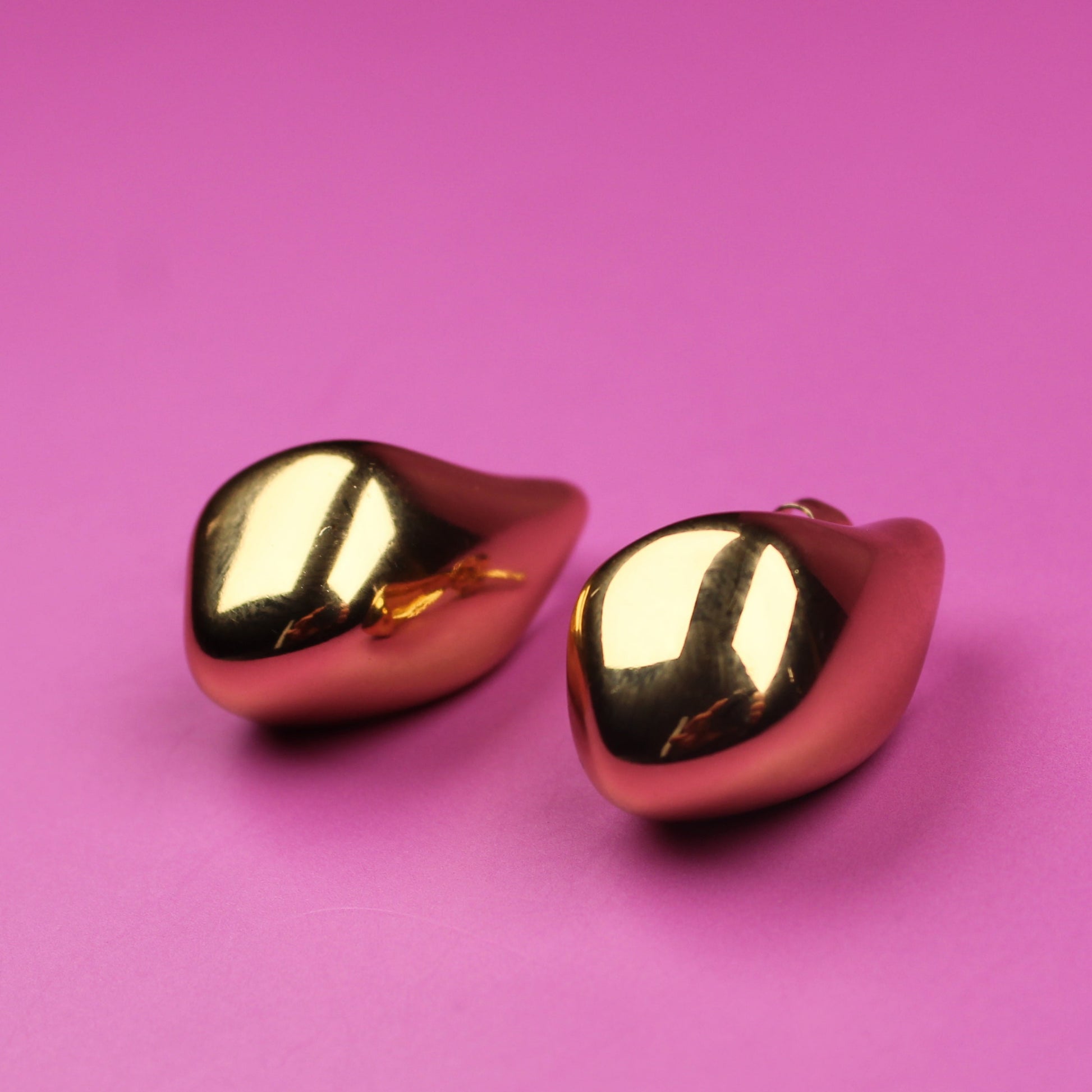 Gold heart-shaped earrings on a pink background
