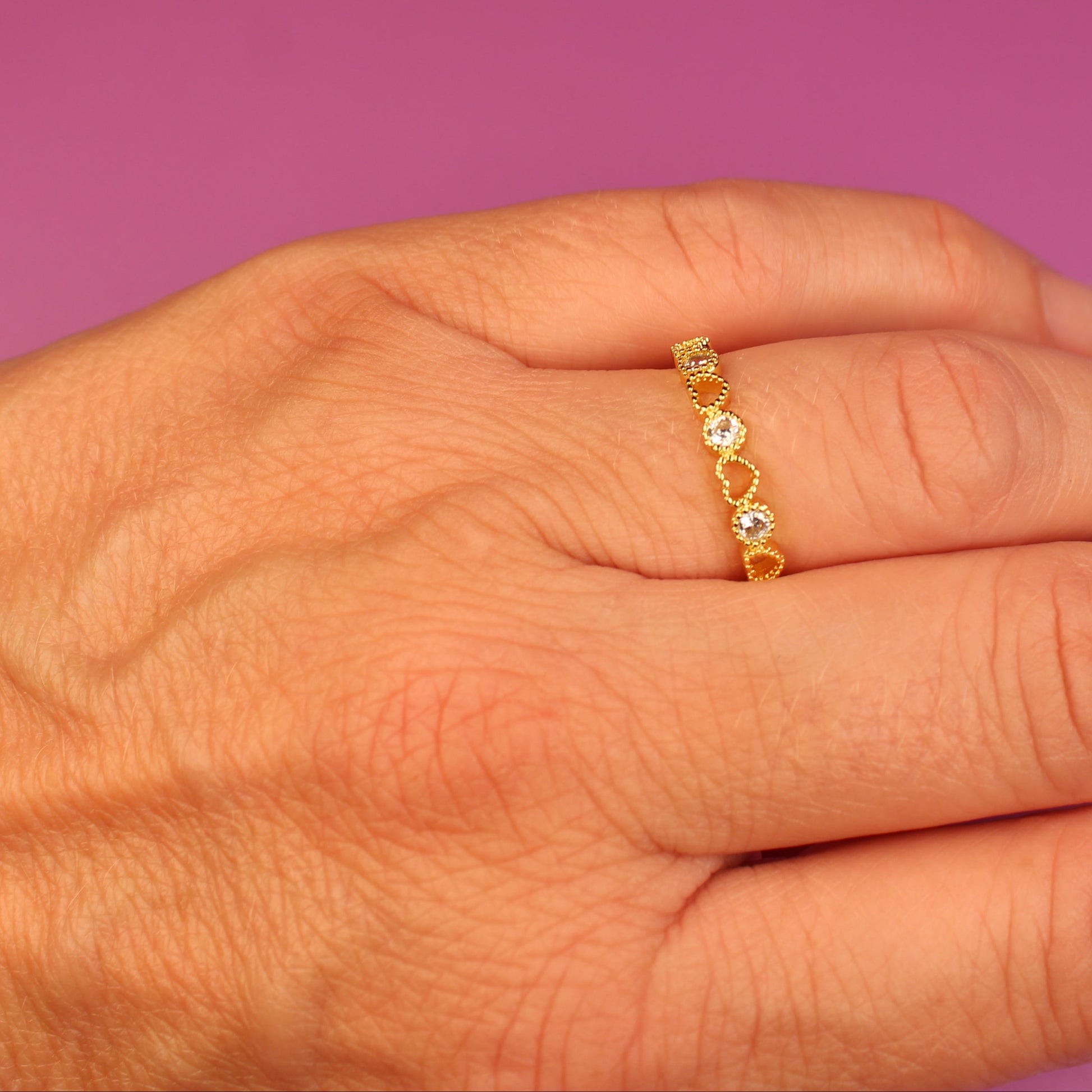Hand wearing a gold ring with small stones on a pink background