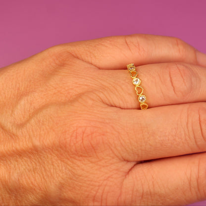 Hand wearing a gold ring with small stones on a pink background
