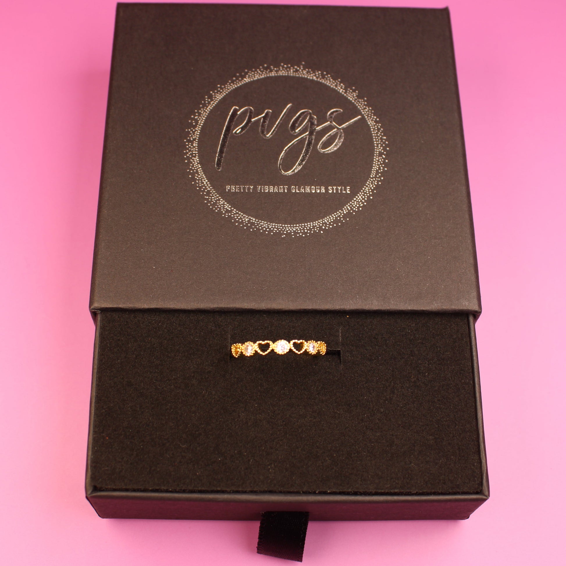 Black jewelry box with a gold necklace on a pink background