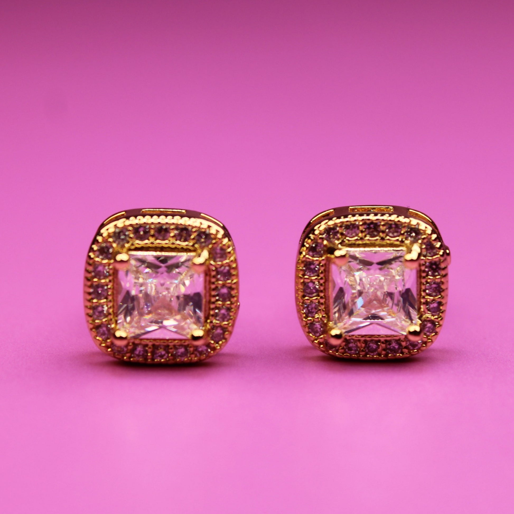 Pair of pink gemstone earrings with gold accents on a pink background