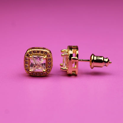 Gold earrings with pink gemstones on a pink background