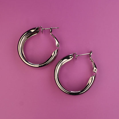 Pair of silver hoop earrings on a pink background