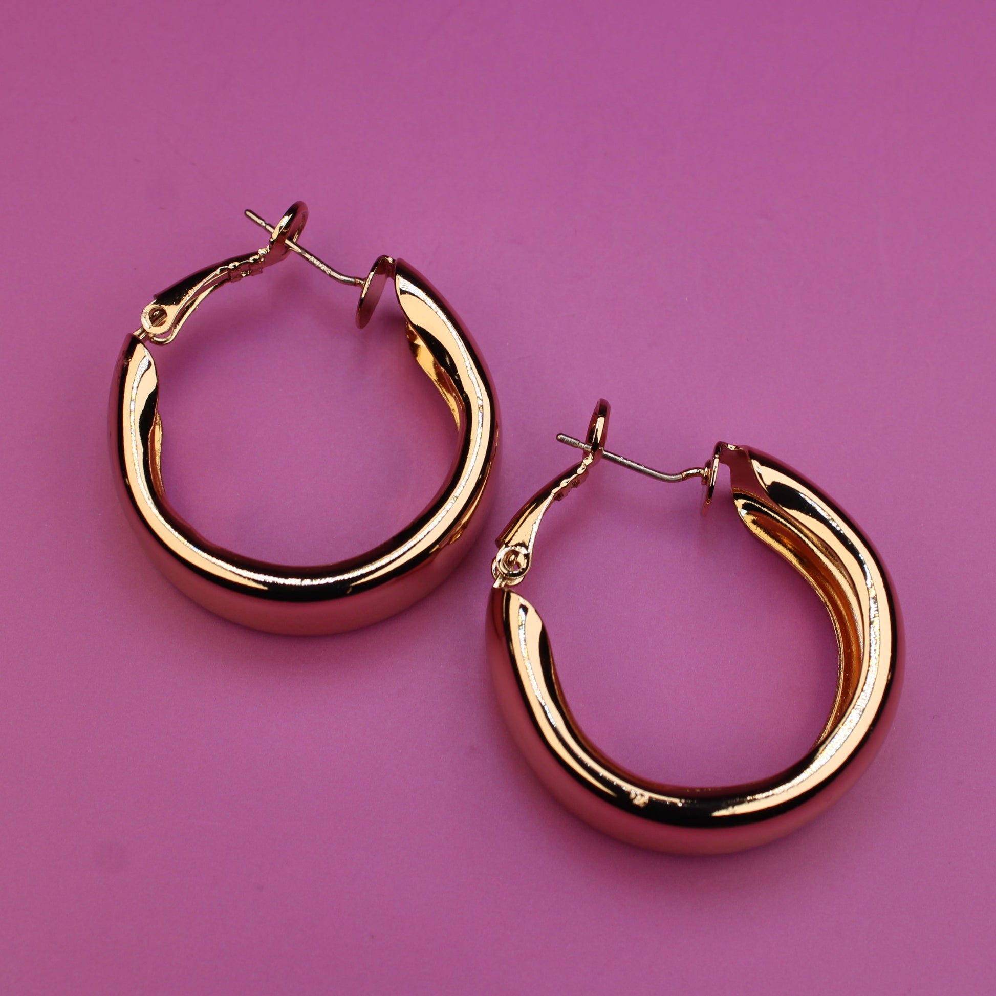 Gold hoop earrings on a pink background