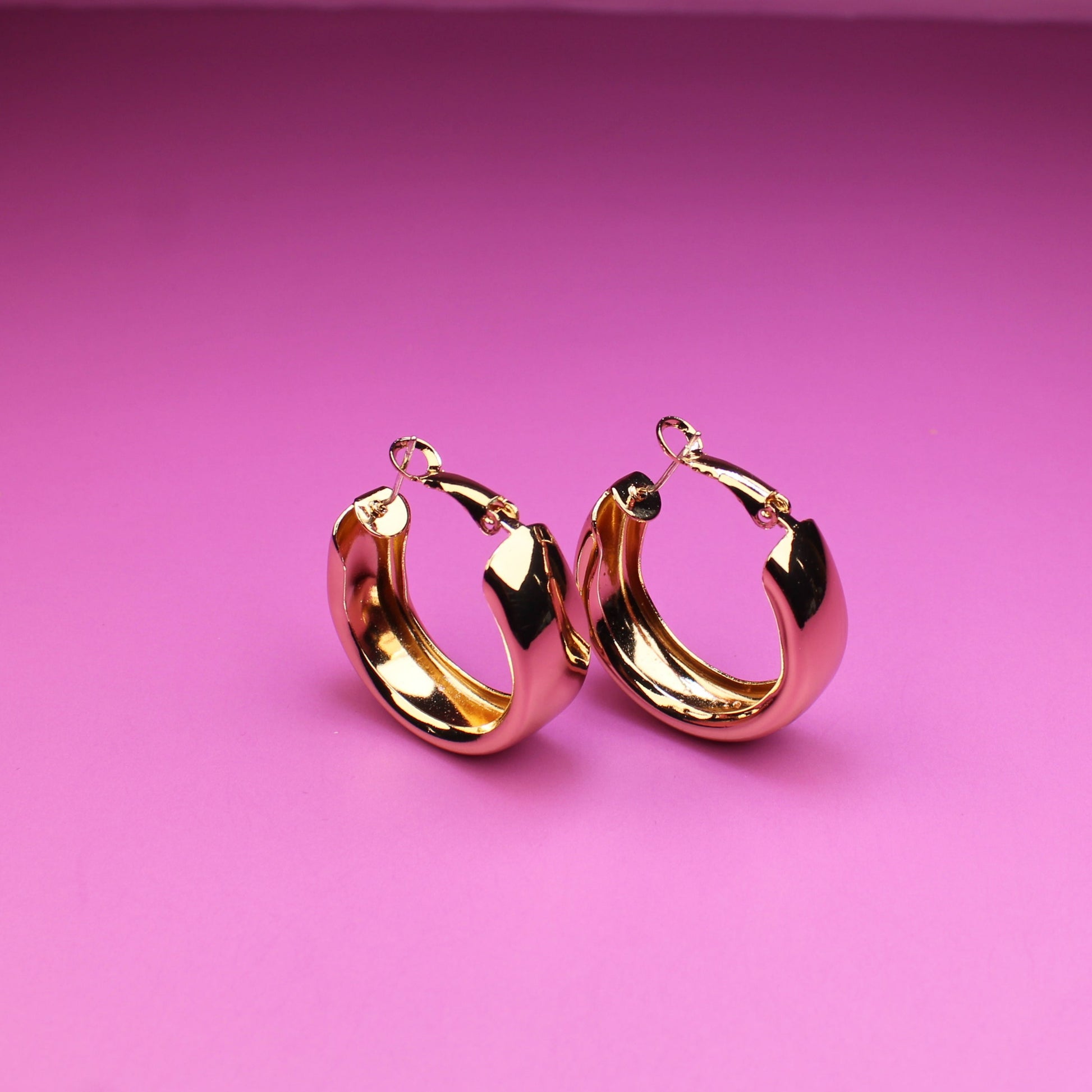 Gold hoop earrings on a pink background