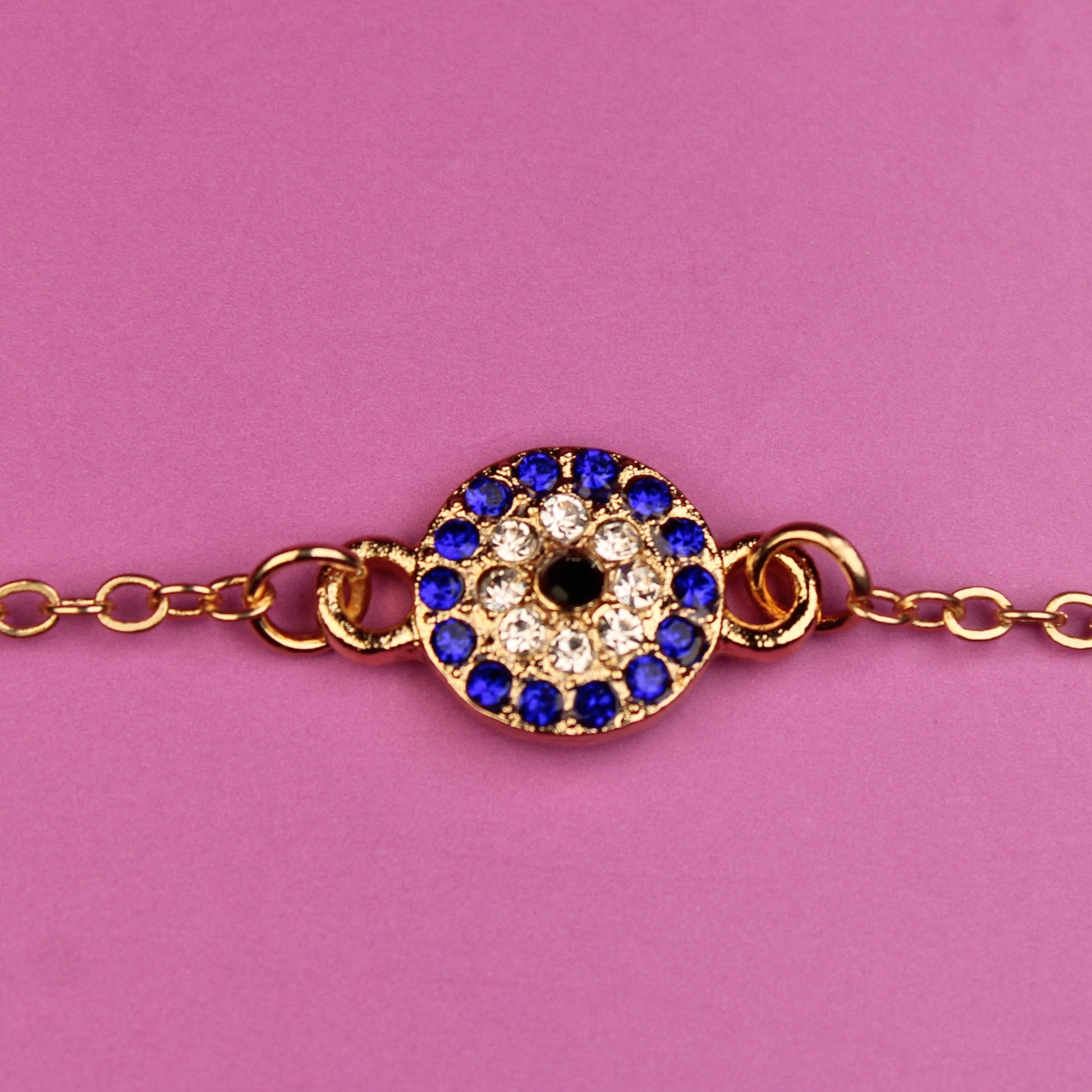 Gold bracelet with a blue and black gemstone on a pink background
