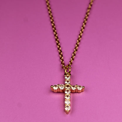Gold cross necklace on a pink background