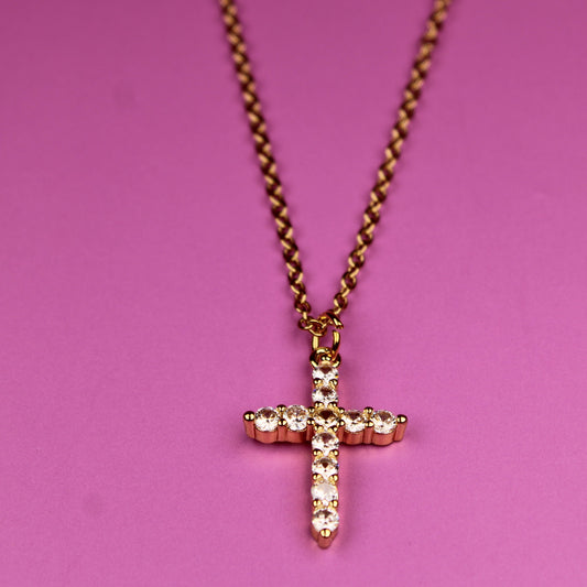 Gold cross necklace on a pink background