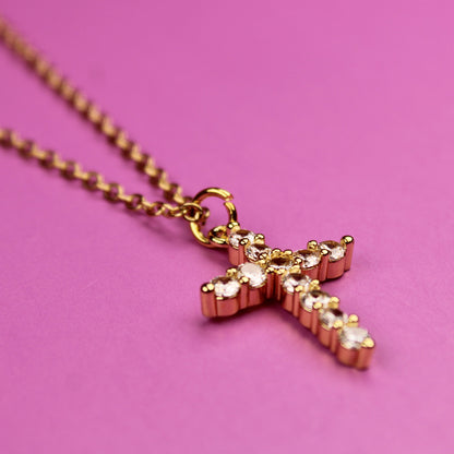 Gold cross necklace on a pink background