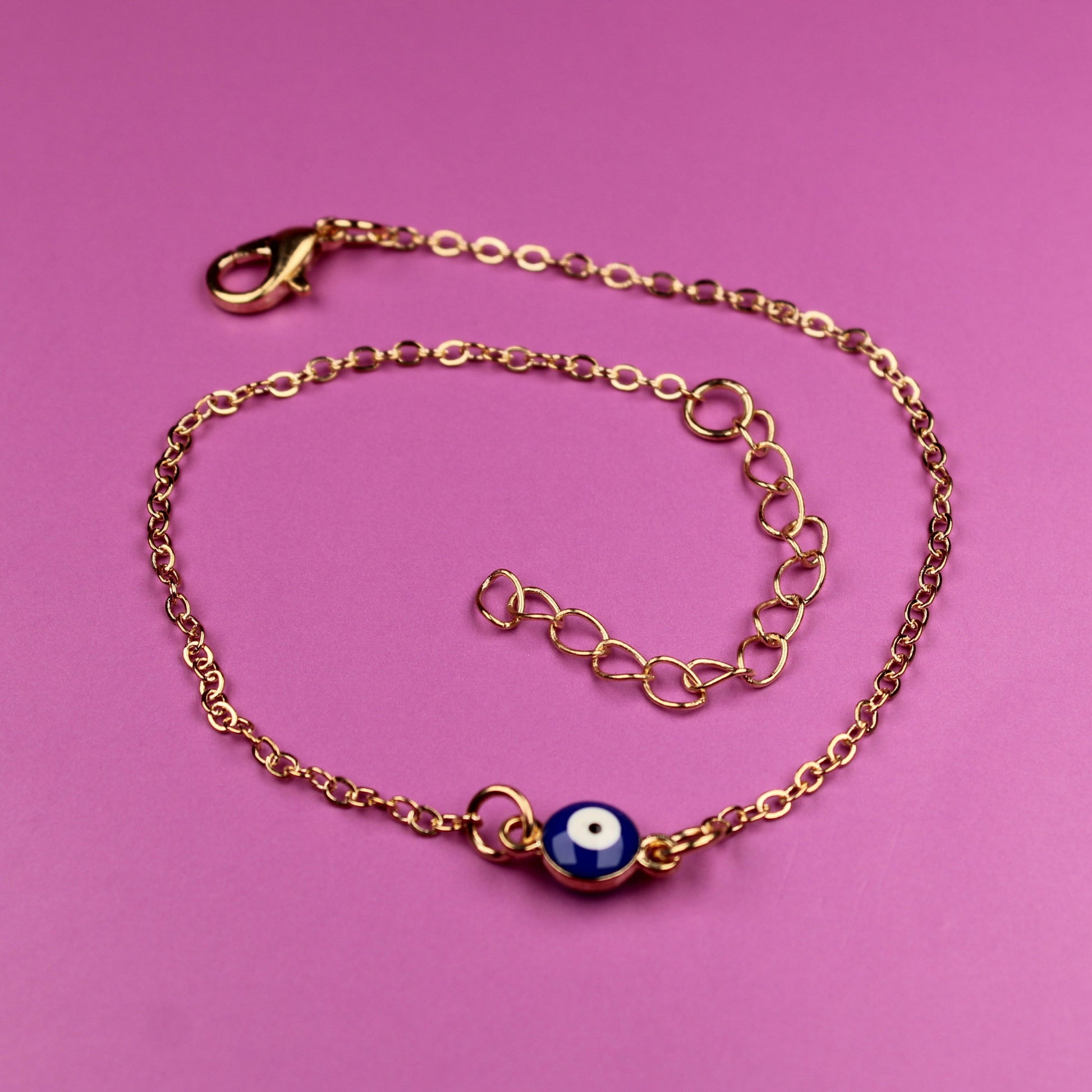 Gold bracelet with a blue charm on a pink background