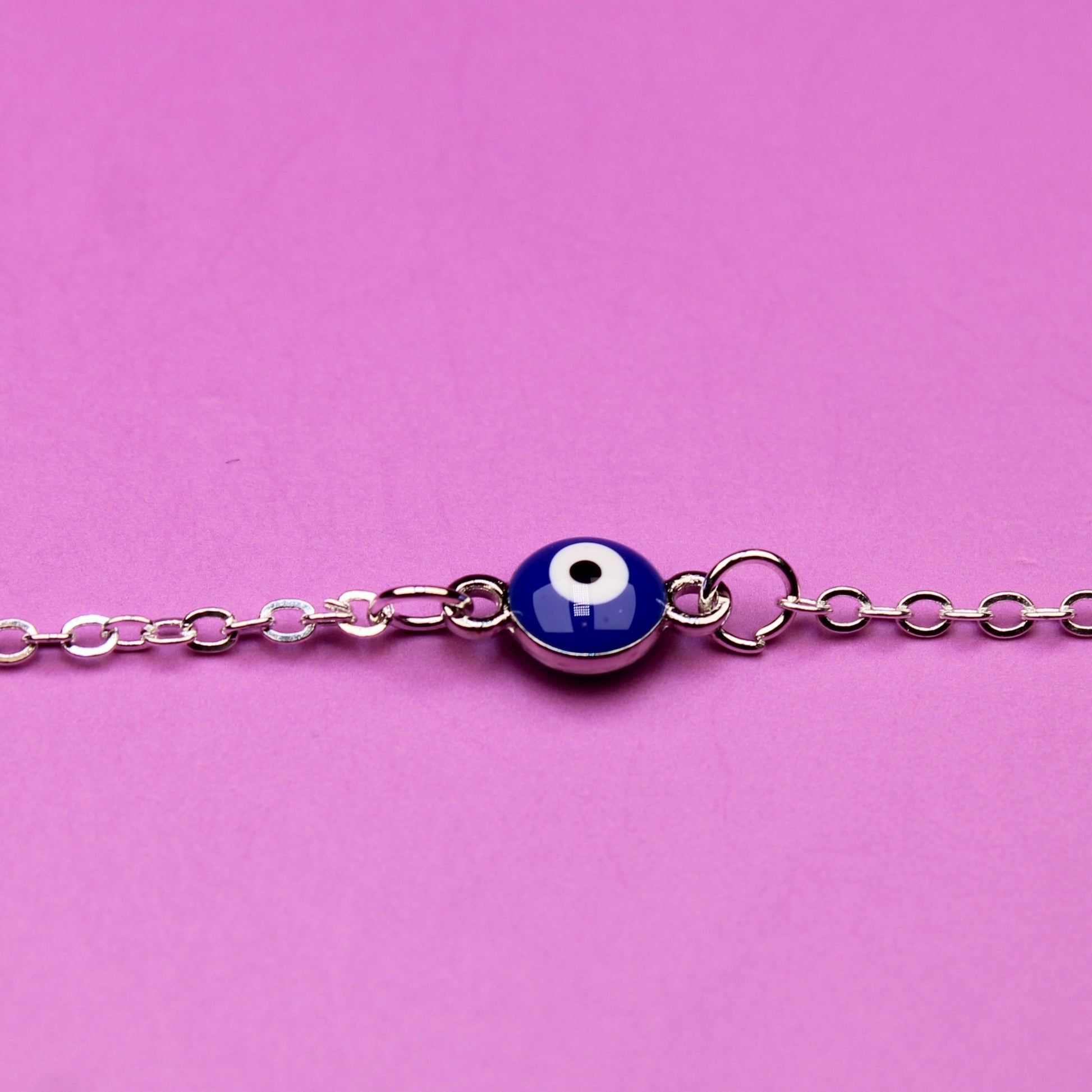 Silver bracelet with a blue evil eye charm on a pink background