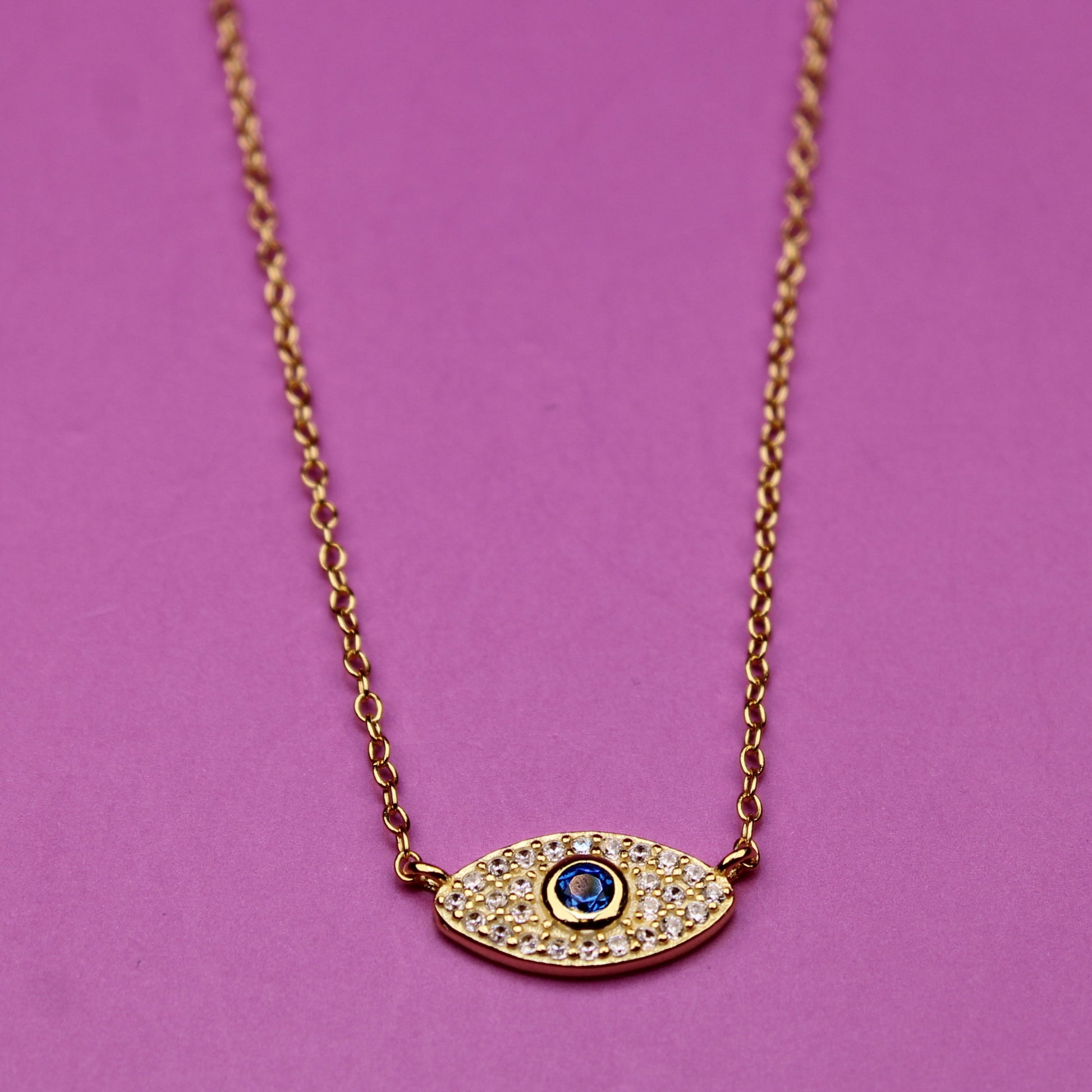 Gold necklace with an eye-shaped pendant on a purple background