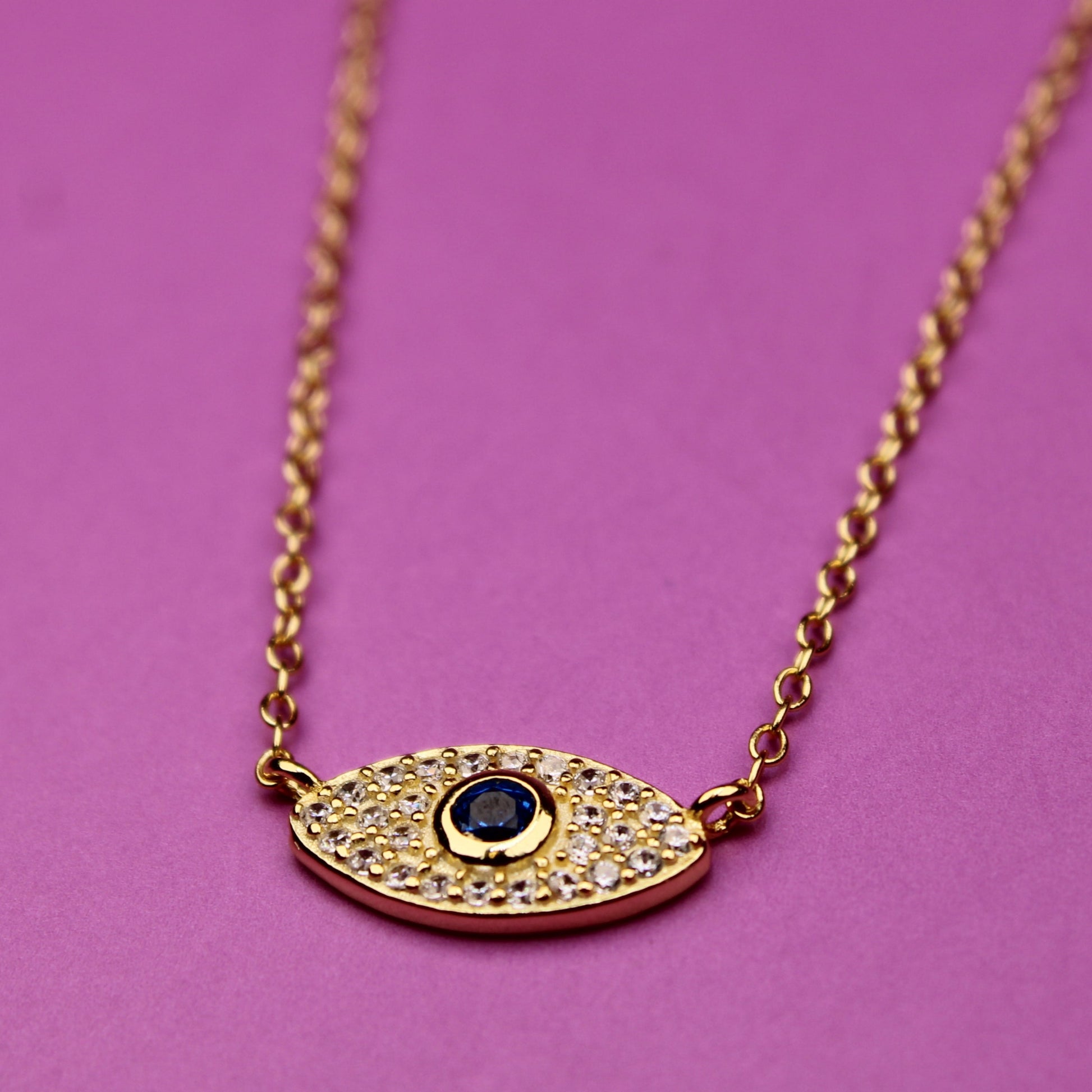 Gold necklace with an eye-shaped pendant on a pink background