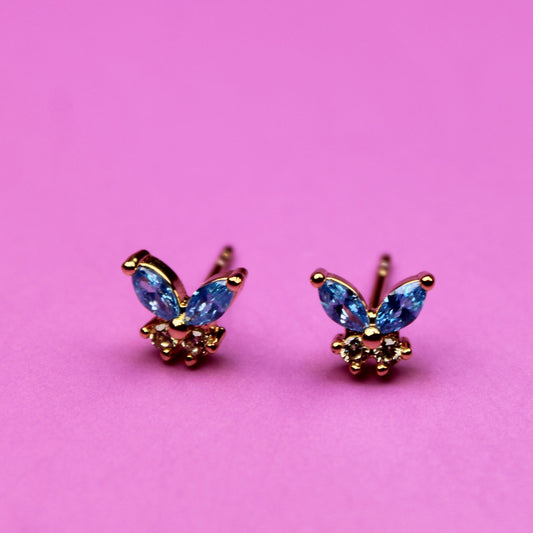Butterfly-shaped earrings with gemstones on a pink background