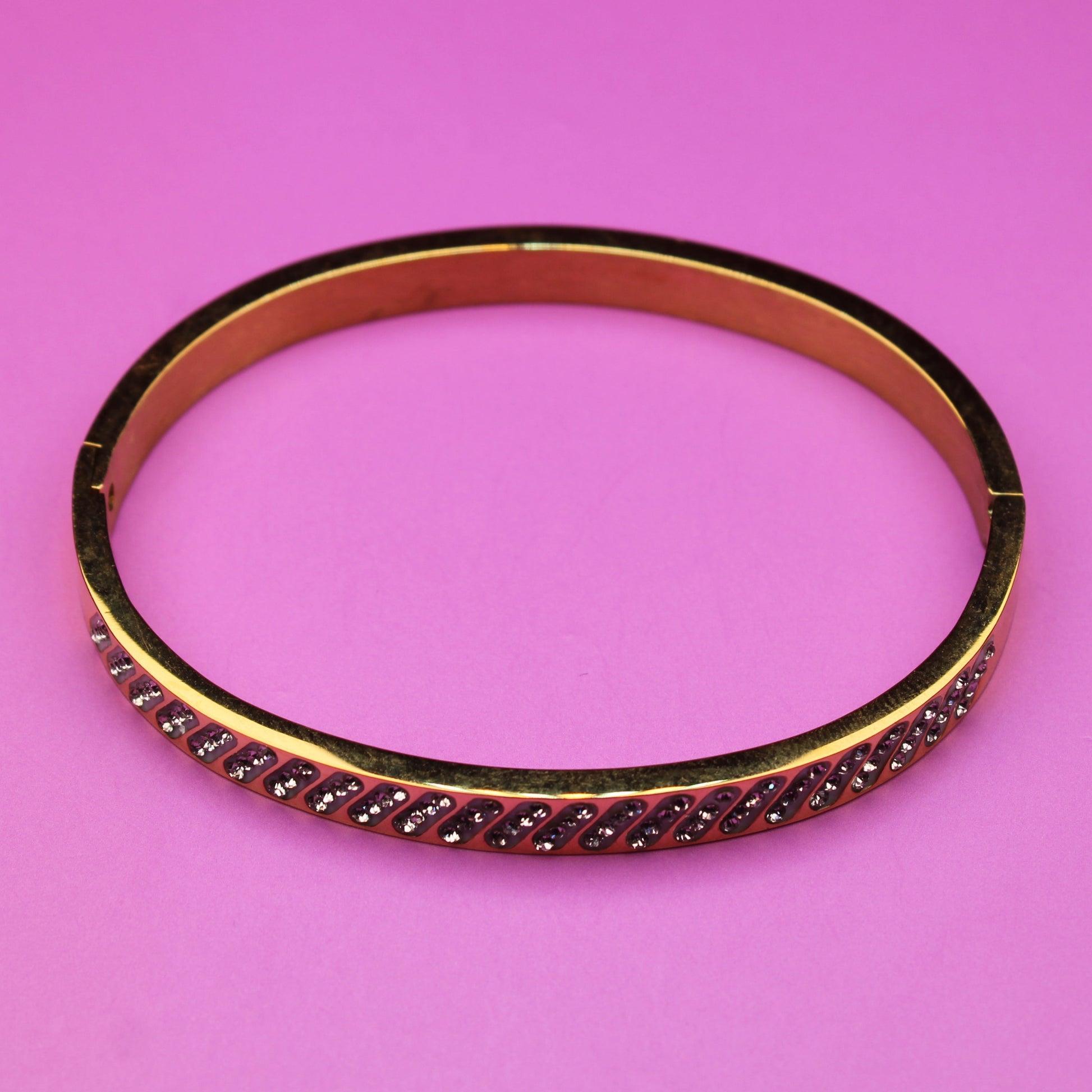 Gold bracelet with red stones on a pink background