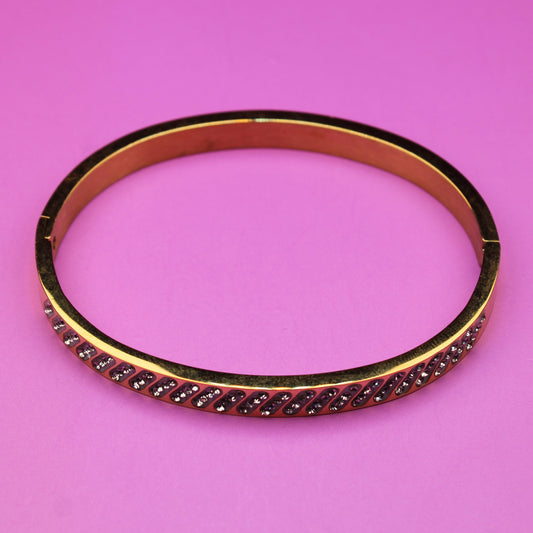 Gold bracelet with red stones on a pink background