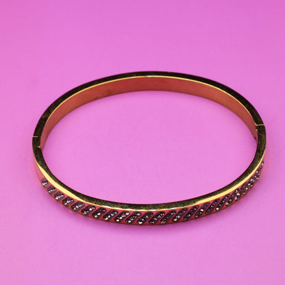 Gold bracelet with red stones on a pink background