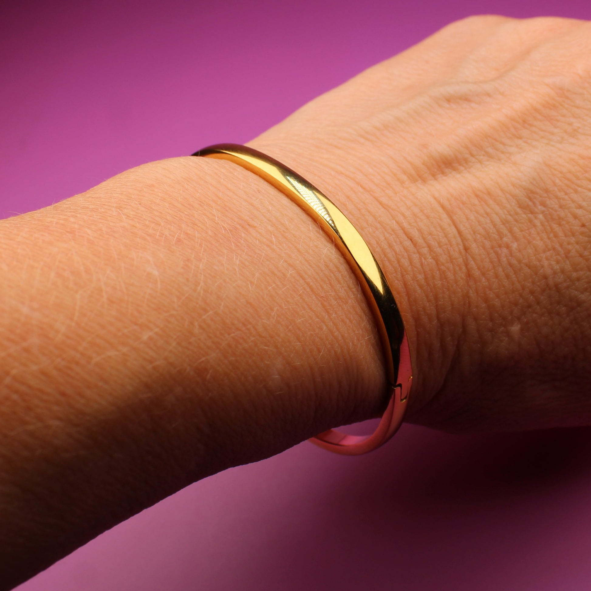 Hand wearing a gold bracelet on a purple surface