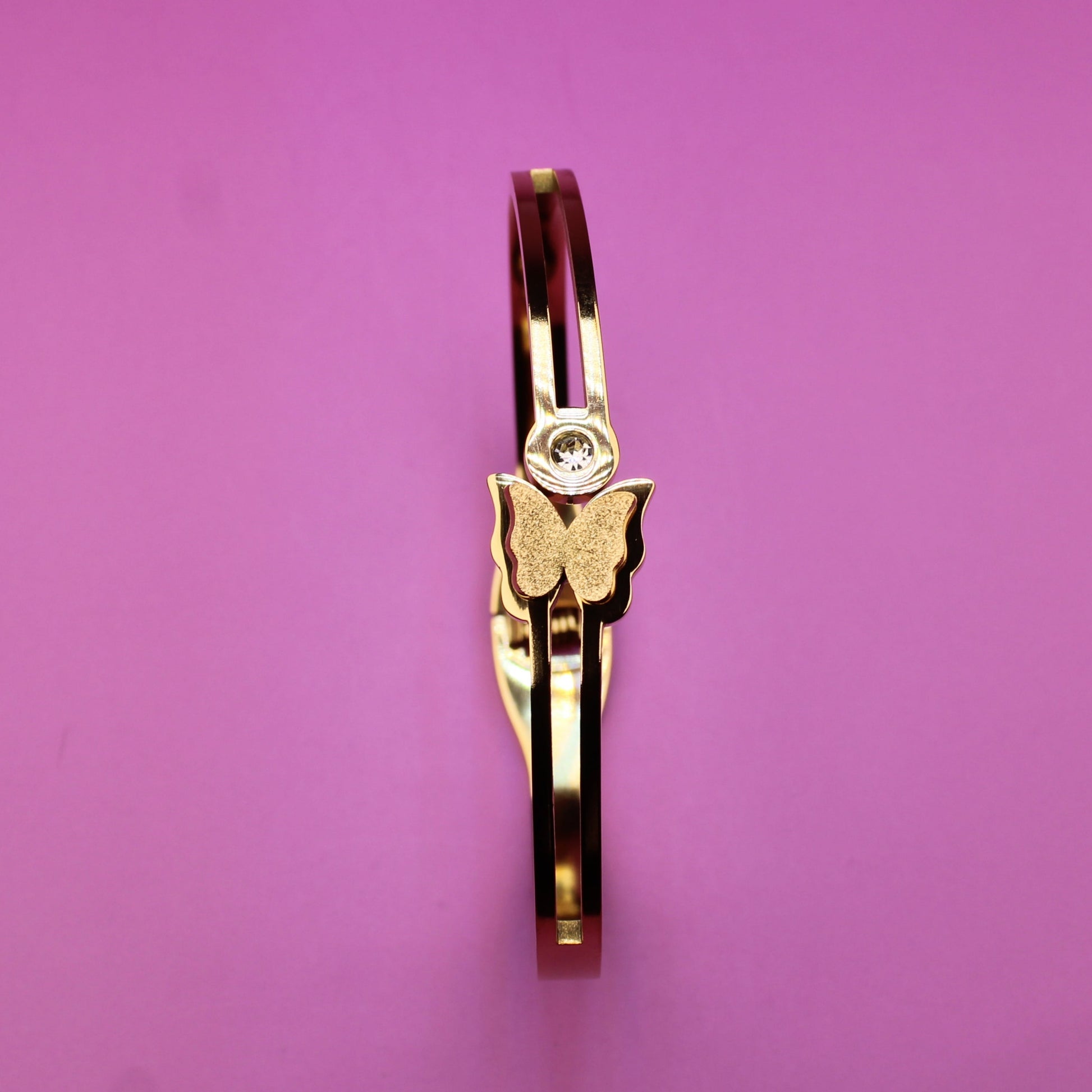 Gold ring with a butterfly design on a pink background