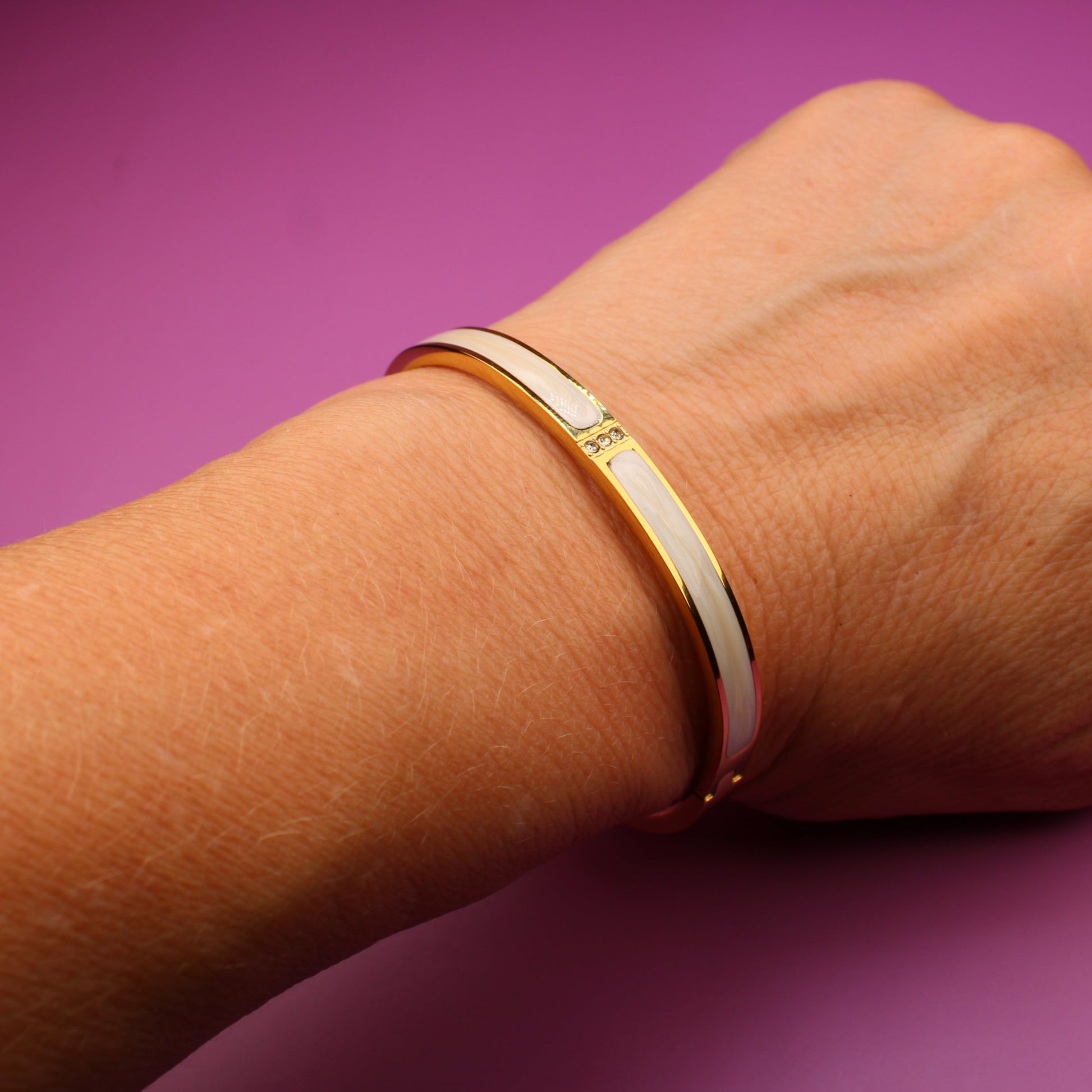 Hand wearing a gold bracelet on a purple background