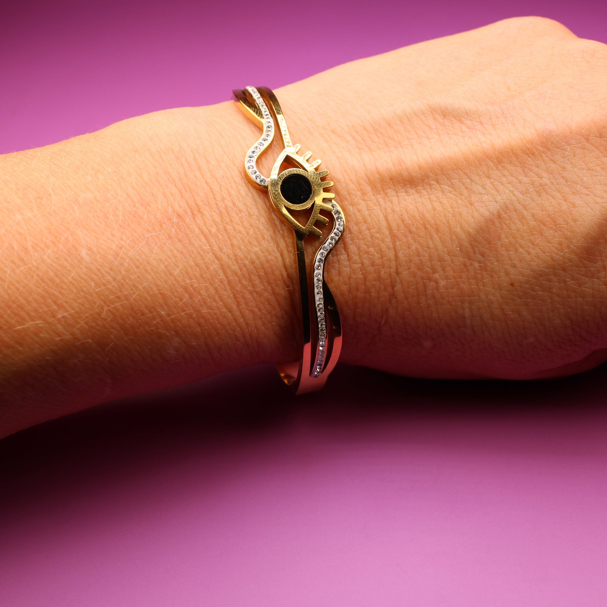 Gold bracelet with a black stone on a wrist against a purple background