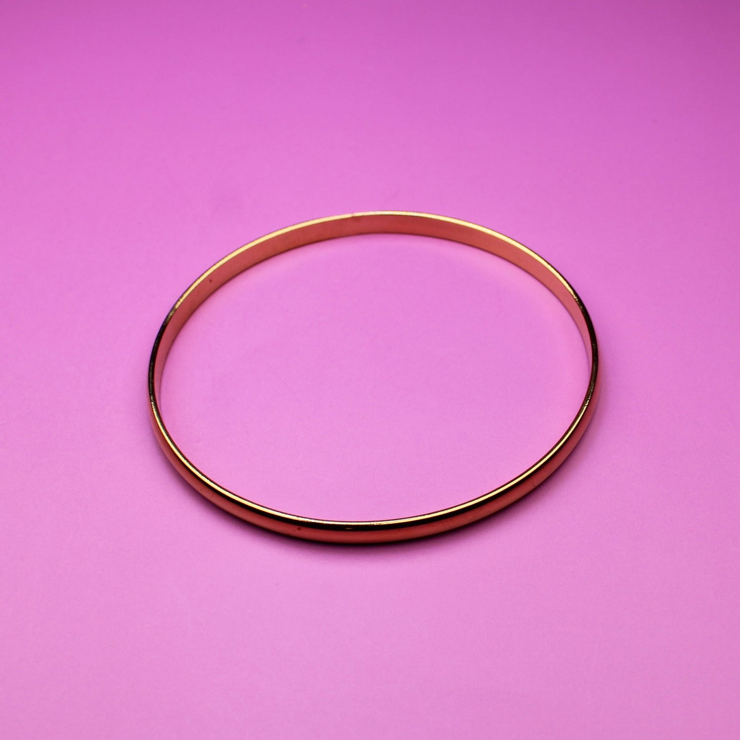 Gold bracelet on a pink surface