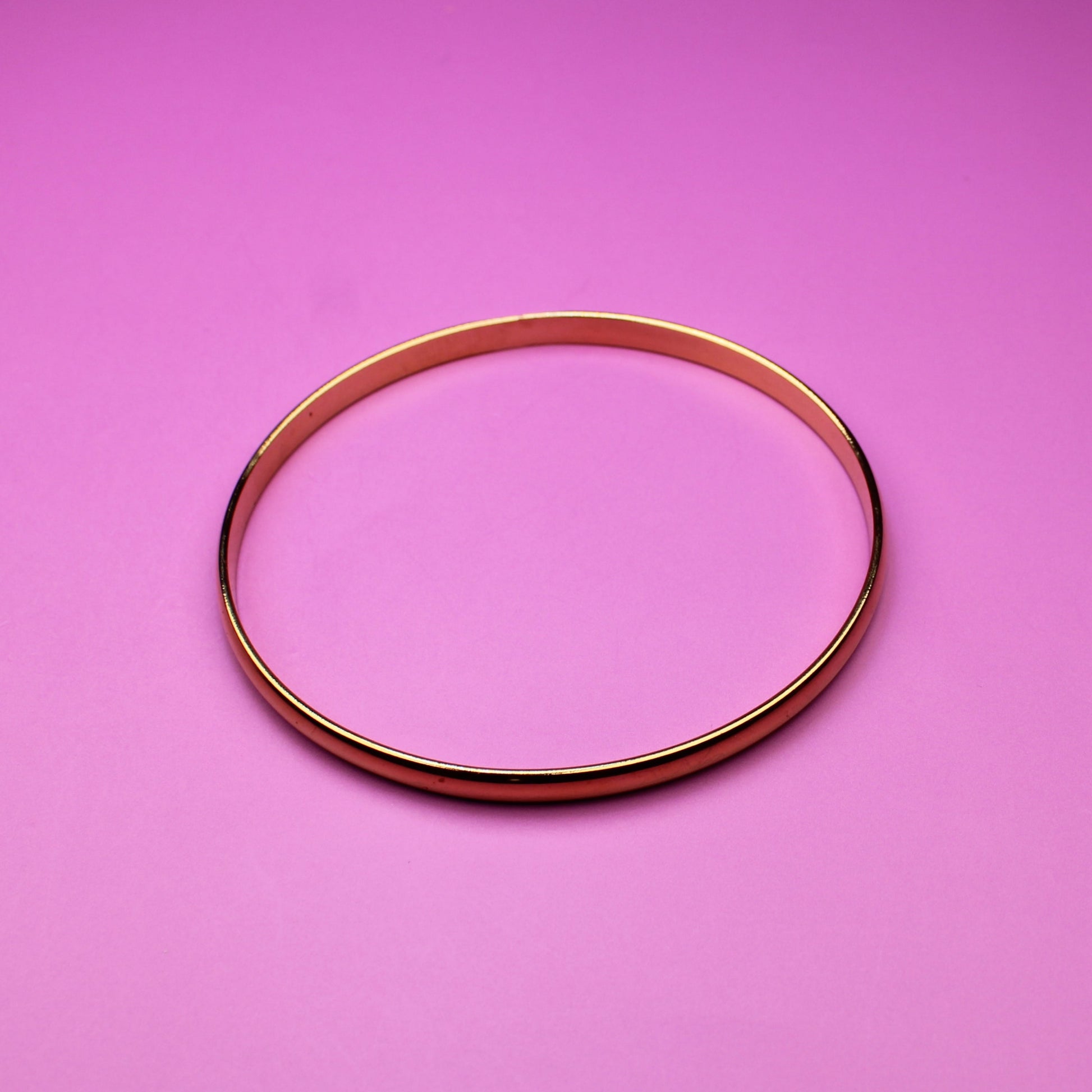 Gold bracelet on a pink surface