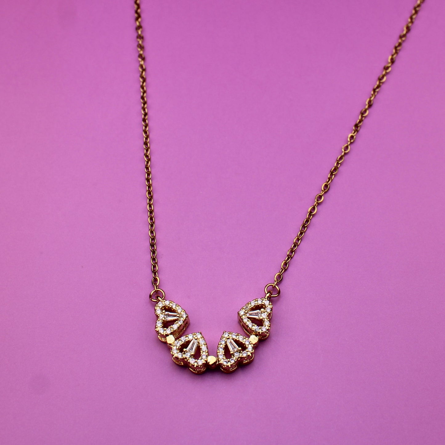Gold necklace with heart-shaped pendants on a pink background