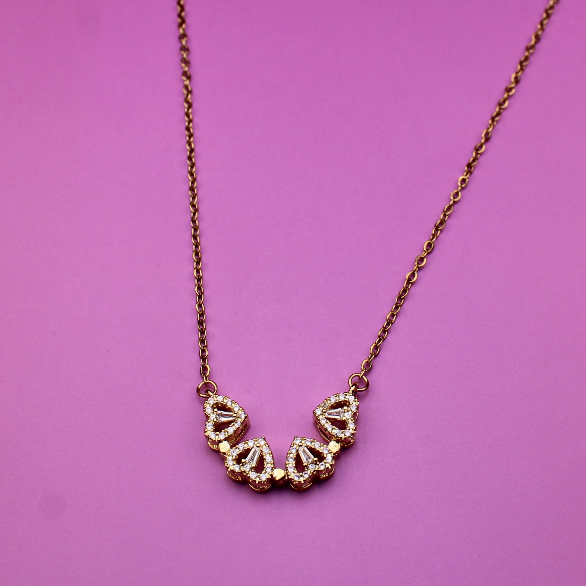 Gold necklace with heart-shaped pendants on a pink background