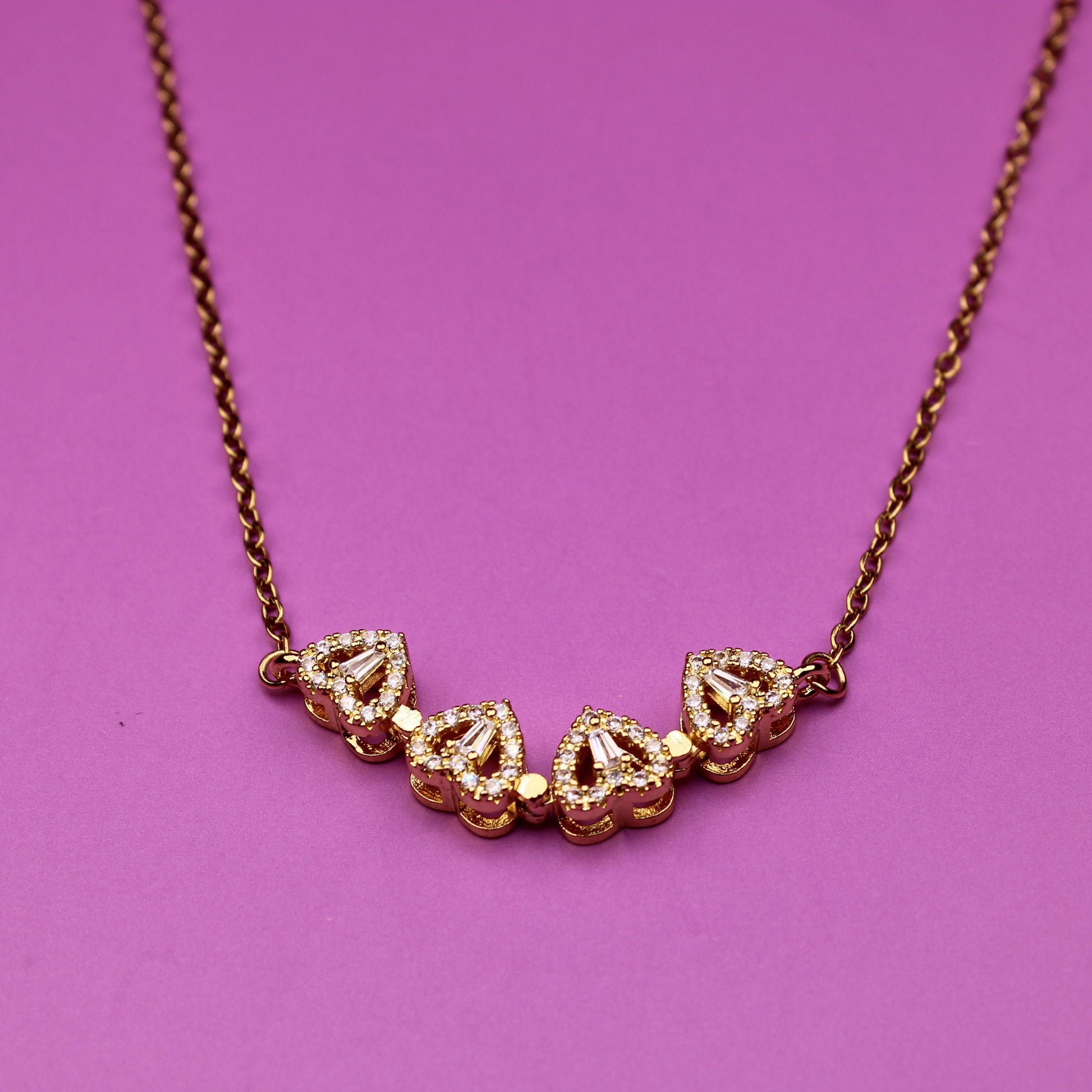 Gold necklace with heart-shaped pendants on a pink background