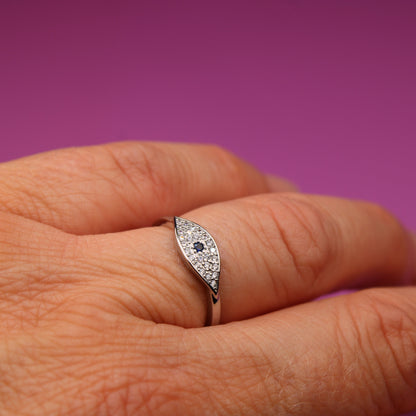 Silver ring with gemstones on a person's finger against a purple background