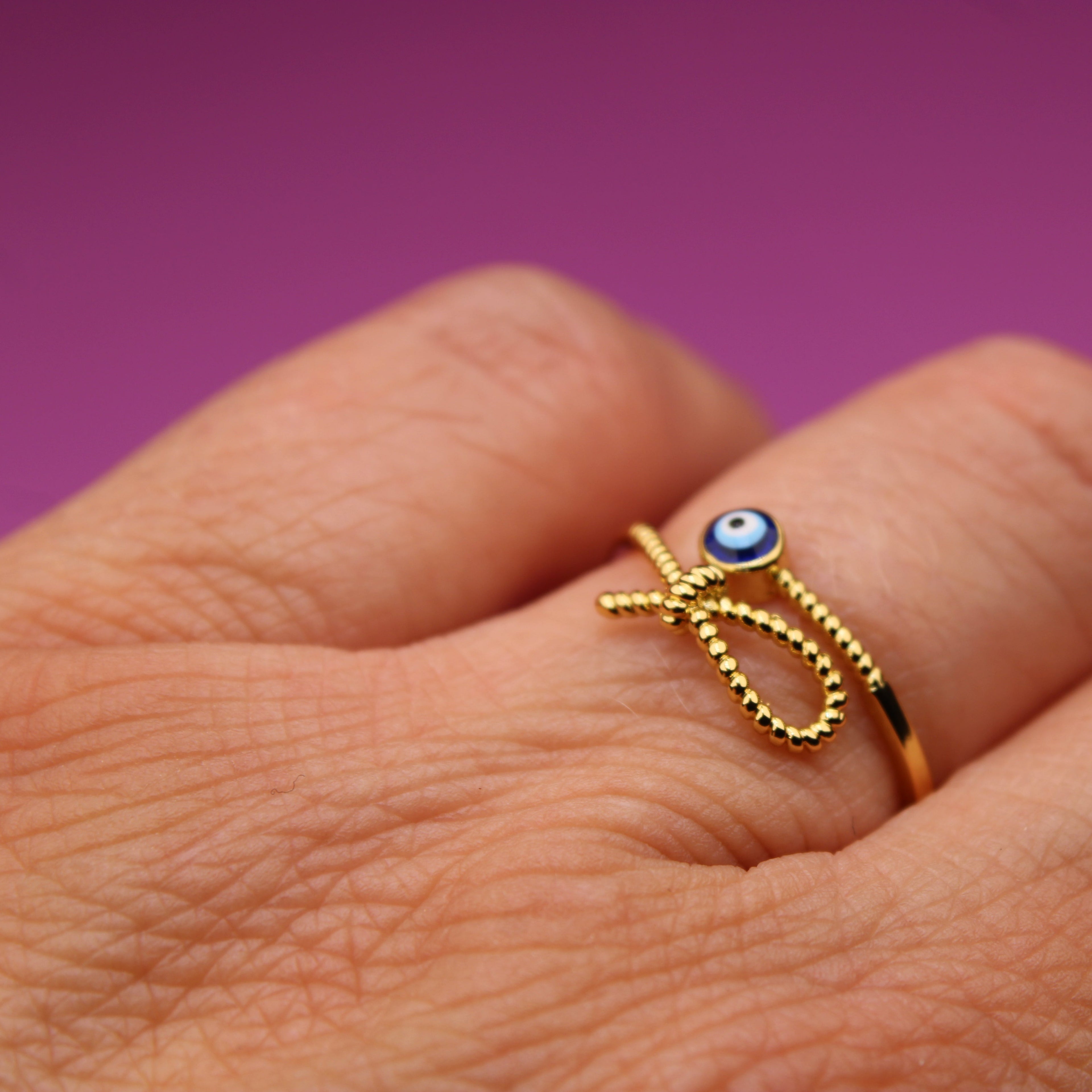 Gold ring with a blue gemstone on a hand against a purple background