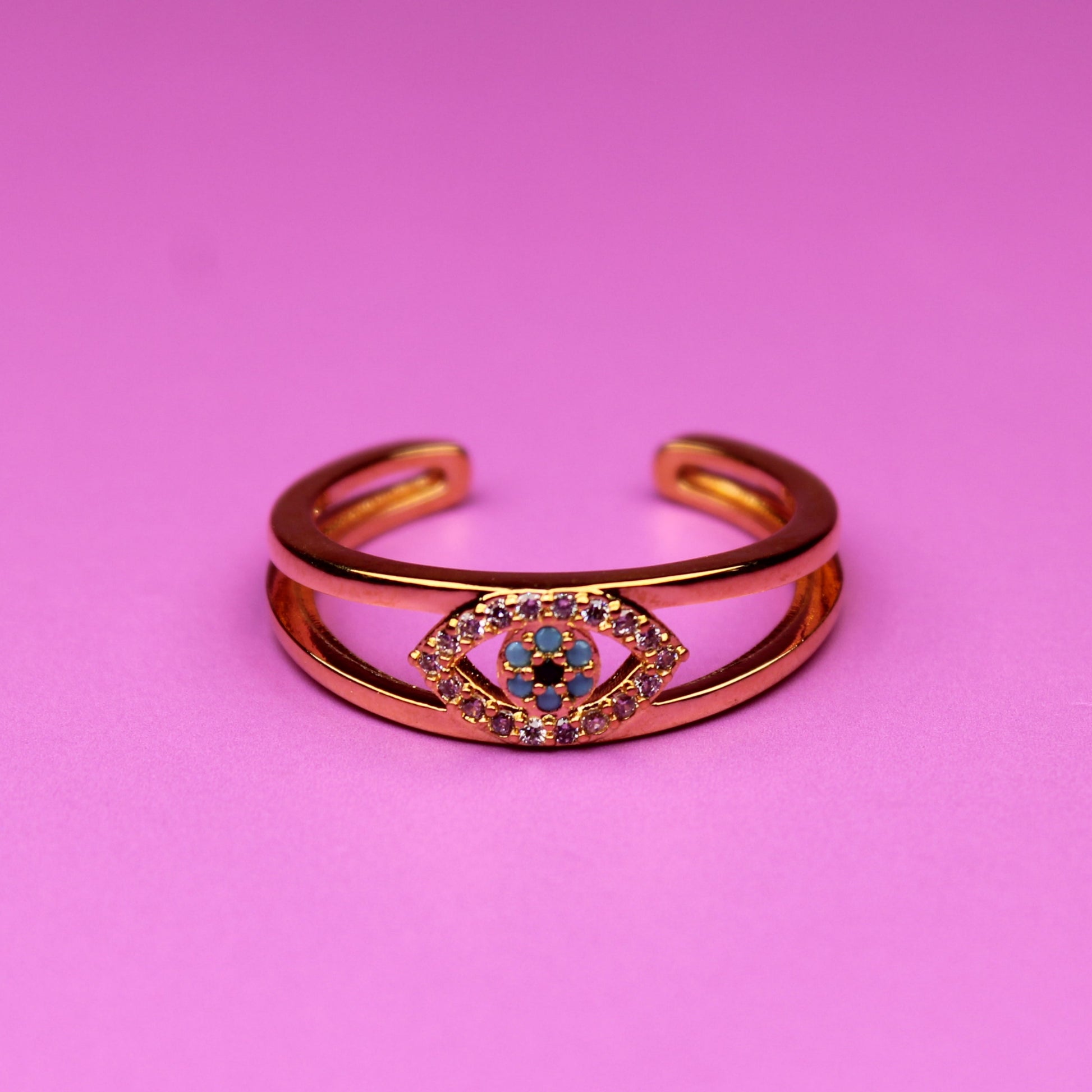 Gold bracelet with a colorful gemstone on a pink background