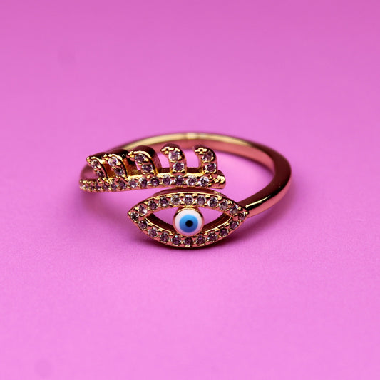 Rose gold ring with eye design on a pink background