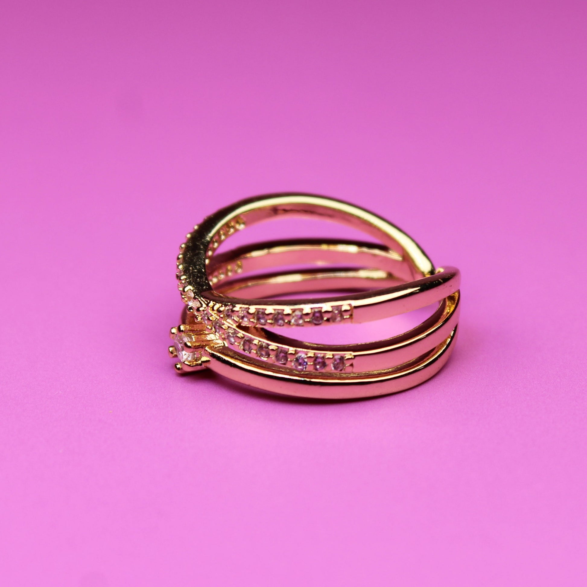 Gold ring with embedded stones on a pink background
