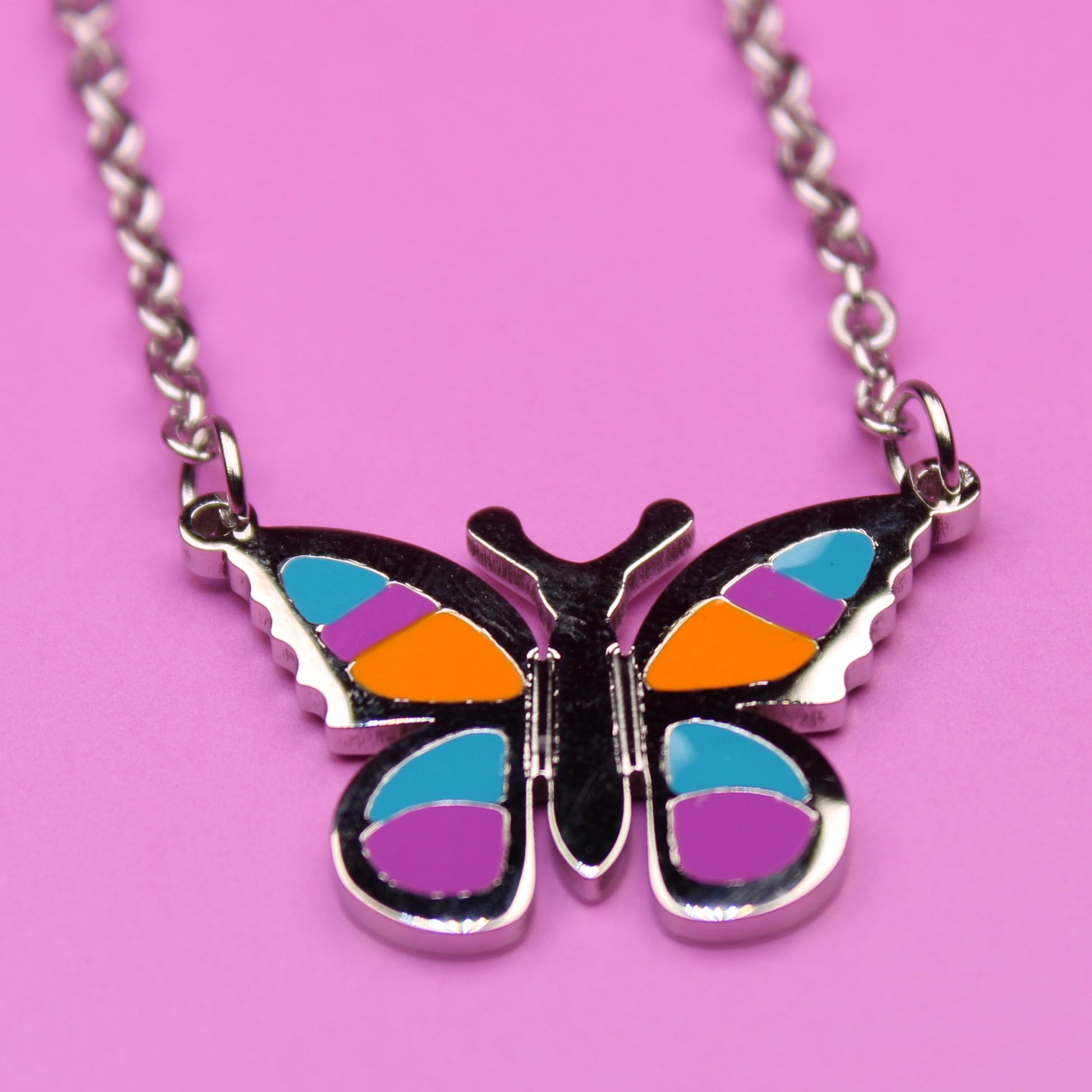 Butterfly-shaped pendant on a chain against a pink background