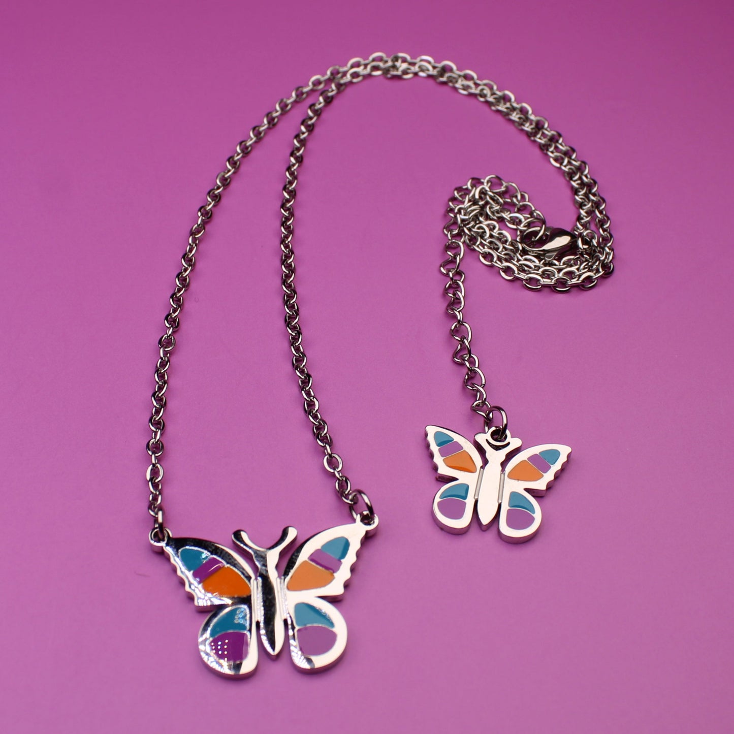 Butterfly-shaped pendant on a chain against a pink background