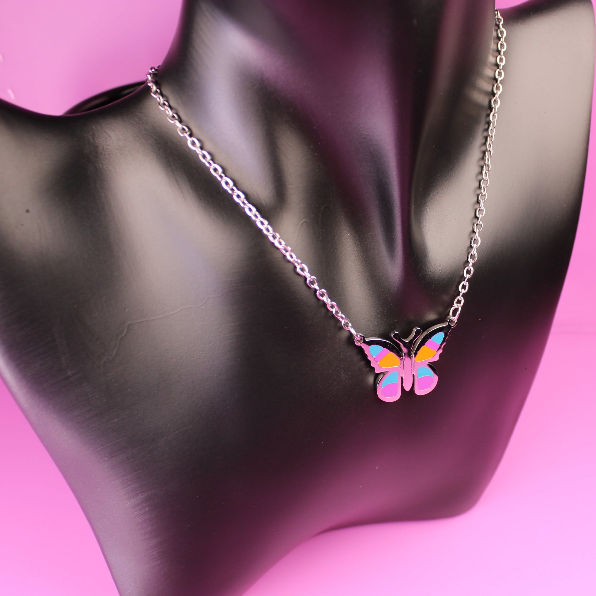 Butterfly-shaped necklace on a black mannequin bust against a pink background
