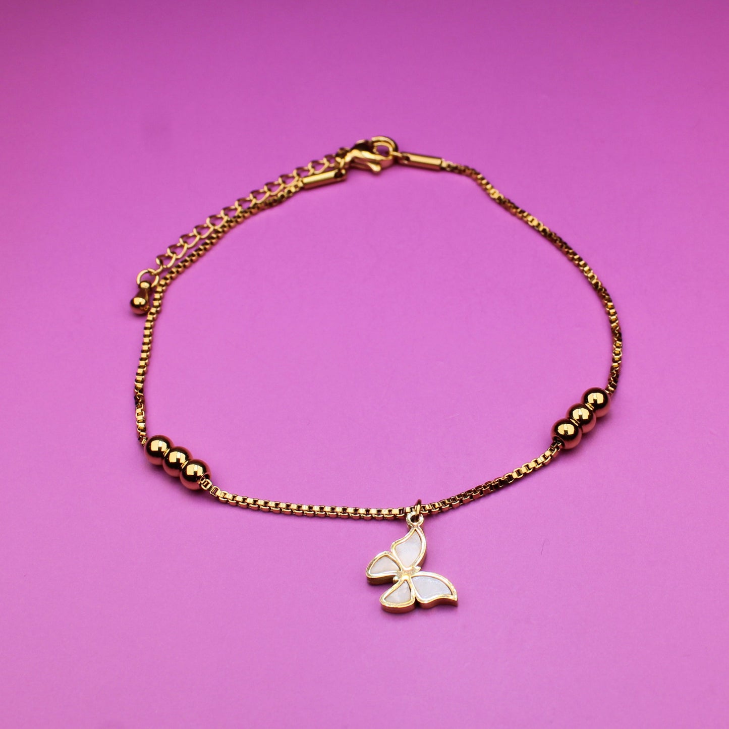 Gold bracelet with a butterfly charm on a pink background