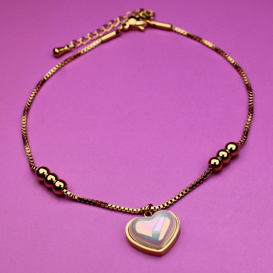 Gold bracelet with a heart-shaped charm on a pink background