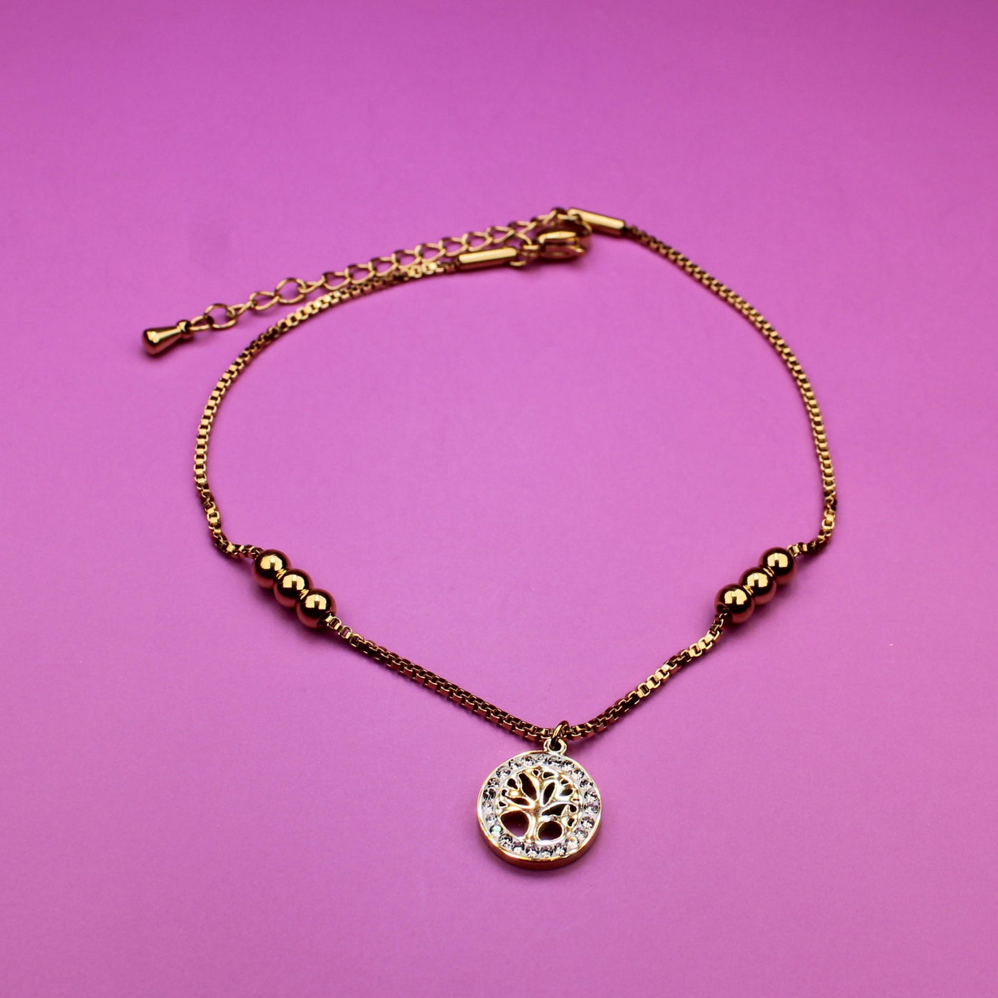 Gold bracelet with a heart-shaped pendant on a pink background