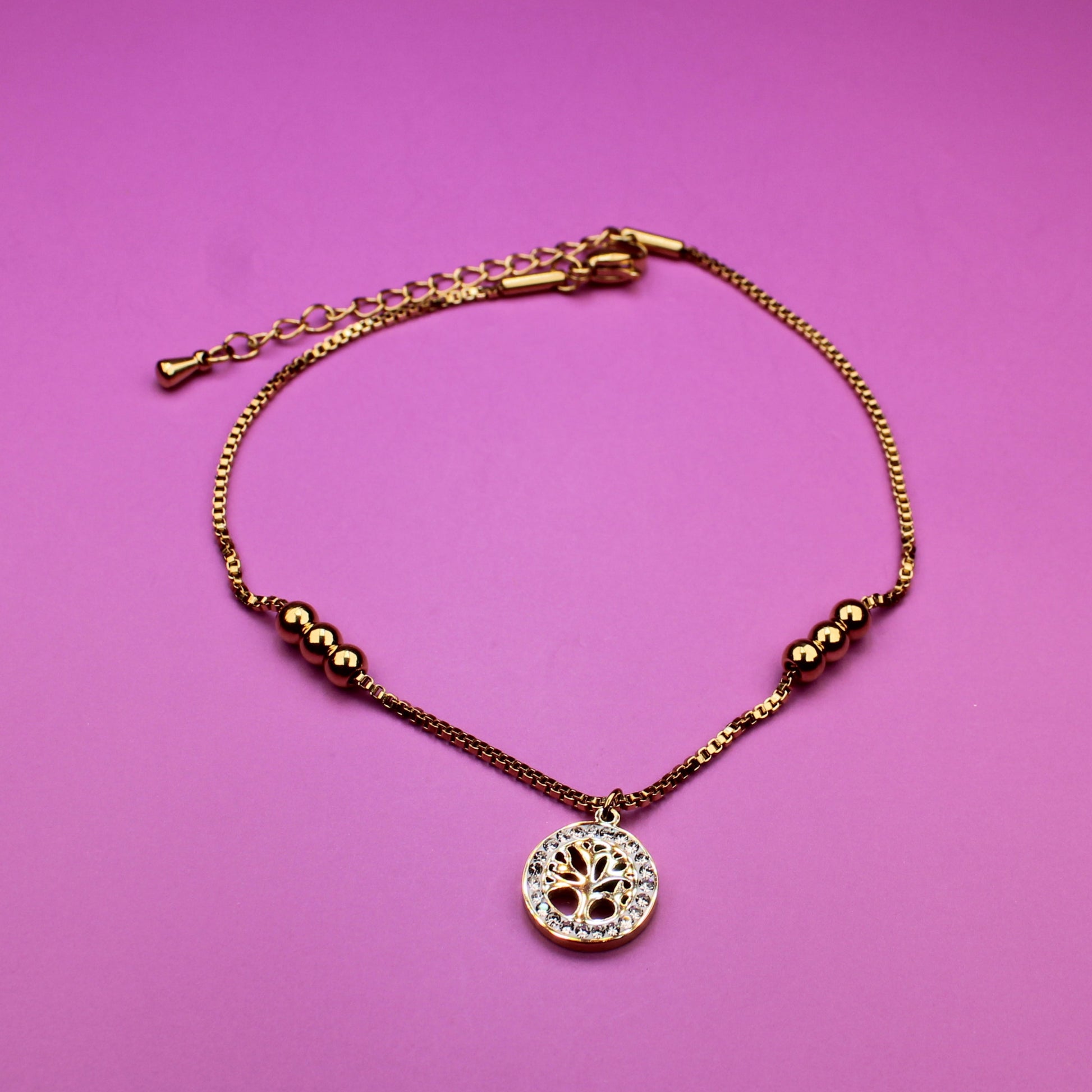 Gold bracelet with a heart-shaped pendant on a pink background
