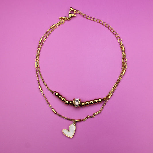 Gold bracelet with heart charm on a pink background