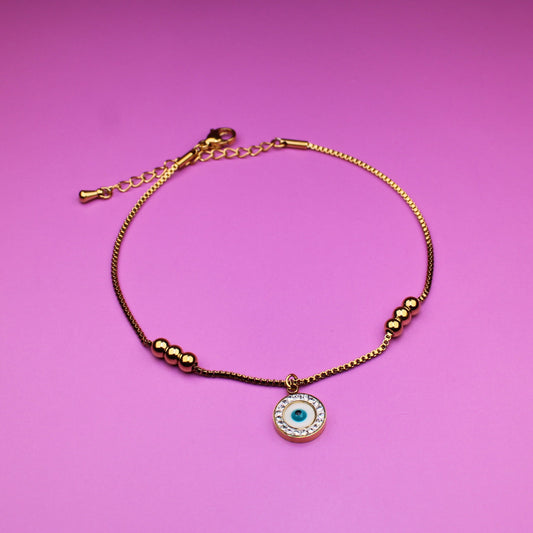 Gold bracelet with a green eye charm on a pink background