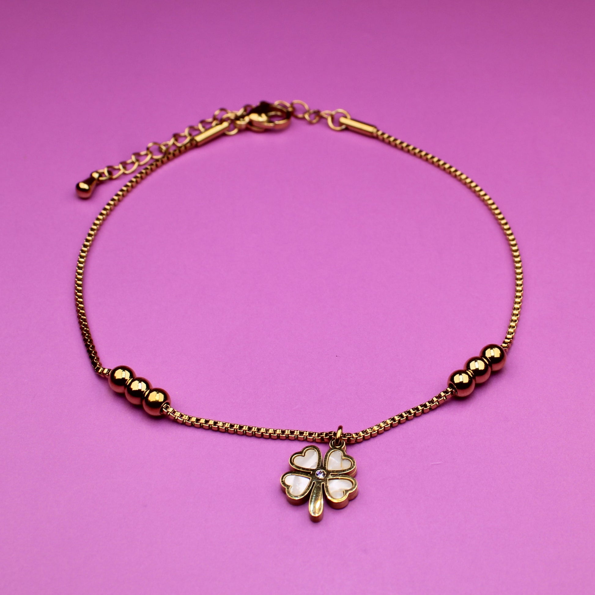 Gold bracelet with a clover charm on a pink background