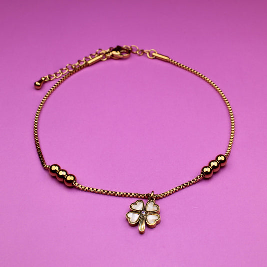 Gold bracelet with a clover charm on a pink background