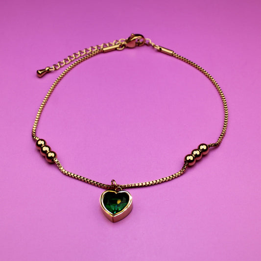 Gold bracelet with a heart-shaped green gemstone on a pink background